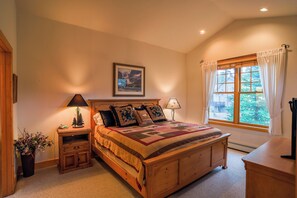 A bedroom with a wooden bed, a nightstand with a lamp, a dresser, a window with curtains, and a framed picture on the wall. - 368 Settlers Drive Private Home with Hot Tub (Breckenridge)