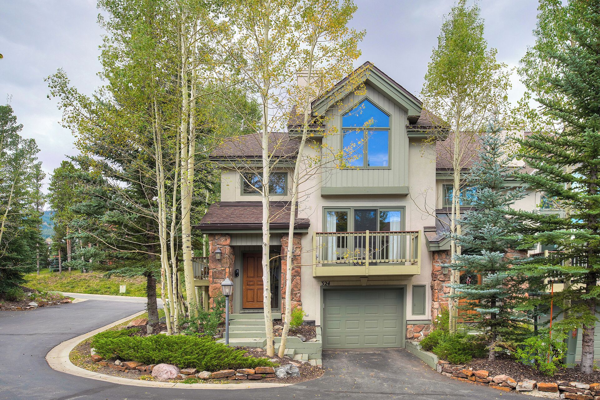 A two-story house with a stone facade, a blue front window, and a green garage door.