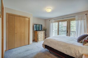 A bedroom with a large bed, a wooden wardrobe, a television on a wooden dresser, and a window with curtains. - Highlander 324 Townhome with Private Hot Tub (Breckenridge)