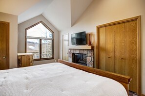 A bedroom with a large bed, a stone fireplace, a TV mounted above it, and a wardrobe. - Highlander 324 Townhome with Private Hot Tub (Breckenridge)