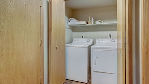 A laundry room with two stacked washers and dryers, wooden flooring, and a shelf above the dryers. - Highlander 324 Townhome with Private Hot Tub (Breckenridge)