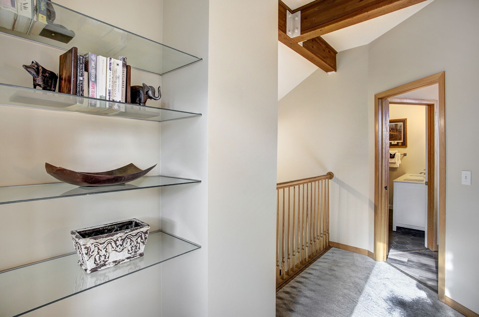 A hallway with a staircase, a wooden railing, and a door leading to a bathroom.