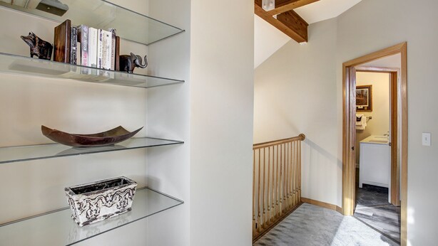 A hallway with a staircase, a wooden railing, and a door leading to a bathroom. - Highlander 324 Townhome with Private Hot Tub (Breckenridge)