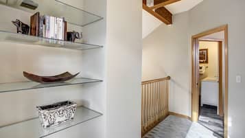 A hallway with a staircase, a wooden railing, and a door leading to a bathroom.