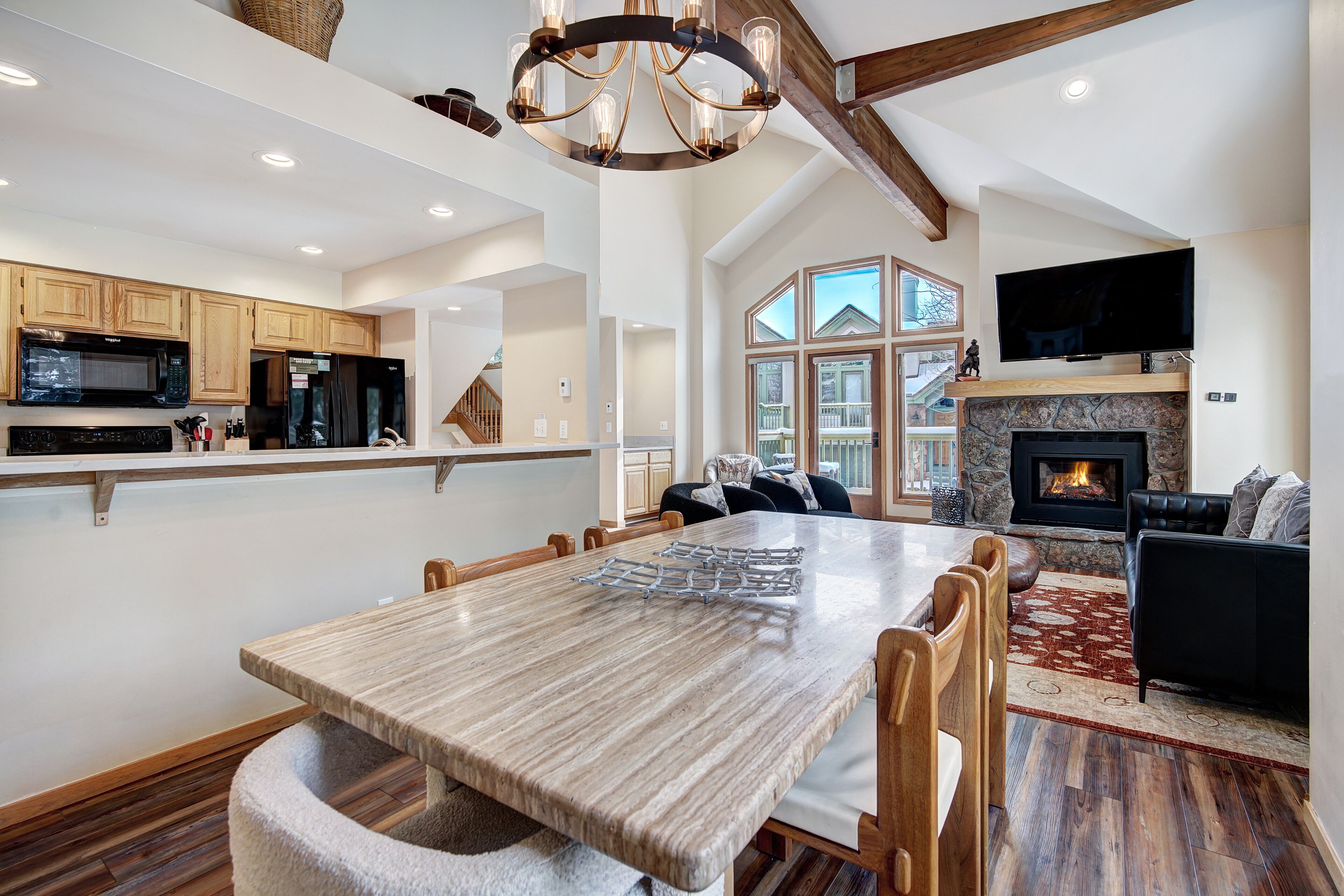 A spacious living area with a large wooden dining table, a fireplace, and a television mounted on the wall.