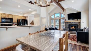A spacious living area with a large wooden dining table, a fireplace, and a television mounted on the wall.