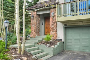 A house with a stone facade, a wooden front door, and a green garage door. - Highlander 324 Townhome with Private Hot Tub (Breckenridge)
