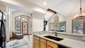A modern kitchen with a large island, wooden cabinets, and a large window. - Highlander 324 Townhome with Private Hot Tub (Breckenridge)