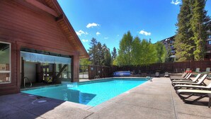 A swimming pool with lounge chairs and a wooden building with a covered entrance. - Highlander 324 Townhome with Private Hot Tub (Breckenridge)