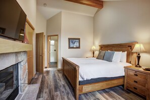 A bedroom with a wooden bed, bedside tables, a lamp, and a fireplace. - Highlander 324 Townhome with Private Hot Tub (Breckenridge)