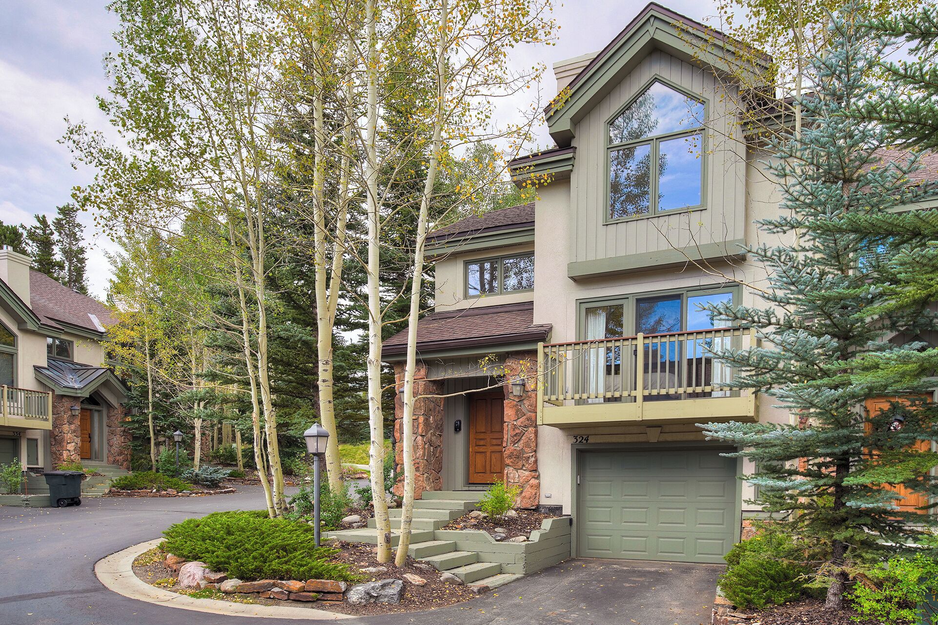 A two-story house with a stone facade, a green garage door, and a balcony with a railing.