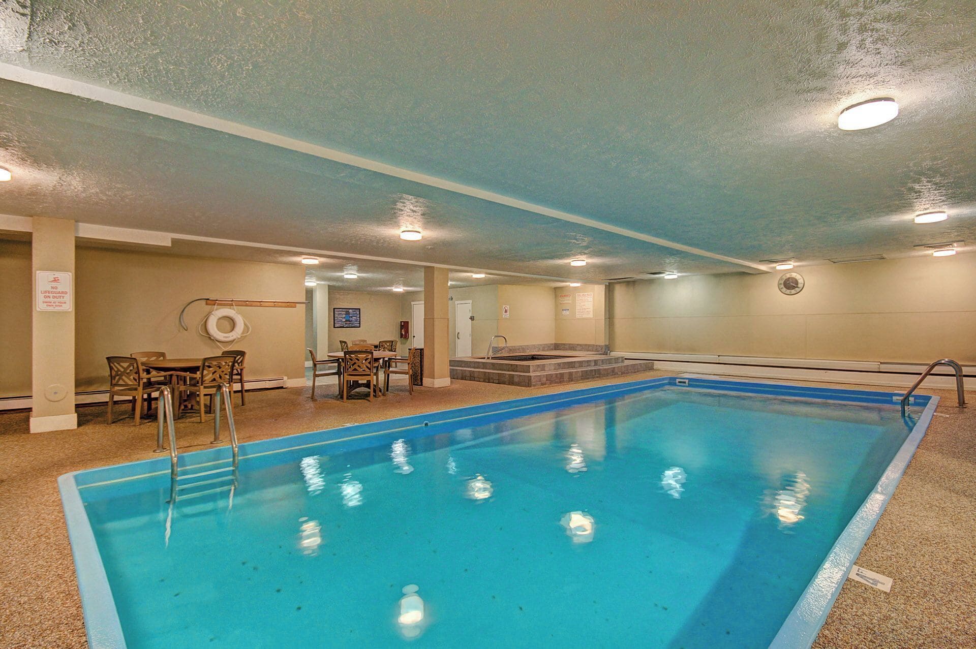 A swimming pool with a lifeguard chair, a table with chairs, and a clock on the wall.