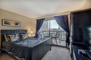 A bedroom with a bed, a TV, a desk, and a view of the outdoors. - Longbranch 201 Condo with Pool & Hot Tub (Breckenridge)