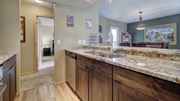 A kitchen with a granite countertop, wooden cabinets, a double sink, and a dining area with a chandelier. - Longbranch 201 Condo with Pool & Hot Tub (Breckenridge)