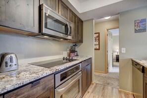 A kitchen with wooden cabinets, a stainless steel microwave, a toaster, and a blender on the countertop. - Longbranch 201 Condo with Pool & Hot Tub (Breckenridge)