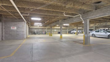 An underground parking garage with concrete pillars, marked parking spaces, and overhead lighting.