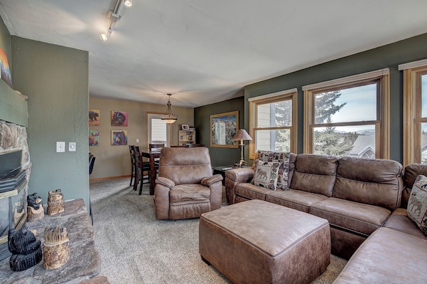 A living room with a leather sofa, ottoman, and a dining area with a table and chairs. There are decorative bear figurines on a shelf and a chandelier above the dining table. - Longbranch 201 Condo with Pool & Hot Tub (Breckenridge)