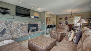 A living room with a stone fireplace, leather furniture, a flat-screen TV, and artwork on the walls. - Longbranch 201 Condo with Pool & Hot Tub (Breckenridge)