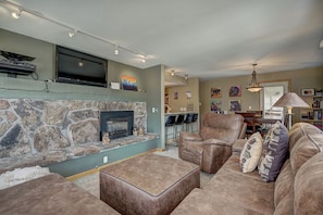A living room with a stone fireplace, leather furniture, a flat-screen TV, and artwork on the walls.