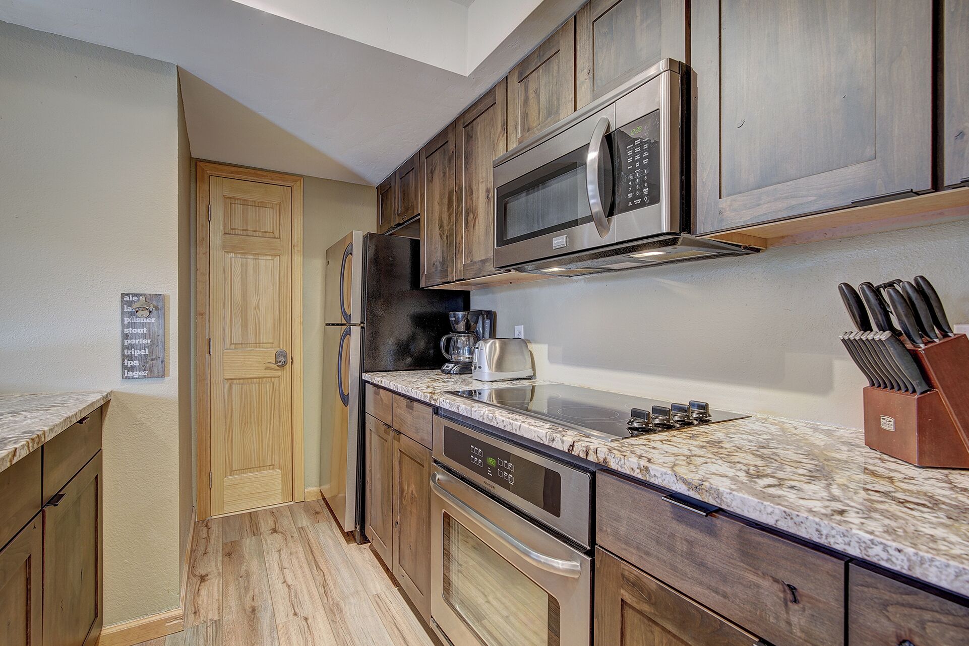 A compact kitchen with wooden cabinets, a stainless steel microwave, a coffee maker, and a knife block.