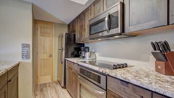 A compact kitchen with wooden cabinets, a stainless steel microwave, a coffee maker, and a knife block.