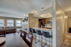 A modern kitchen with a central island, bar stools, and a dining area with a sofa and chairs. - Longbranch 201 Condo with Pool & Hot Tub (Breckenridge)