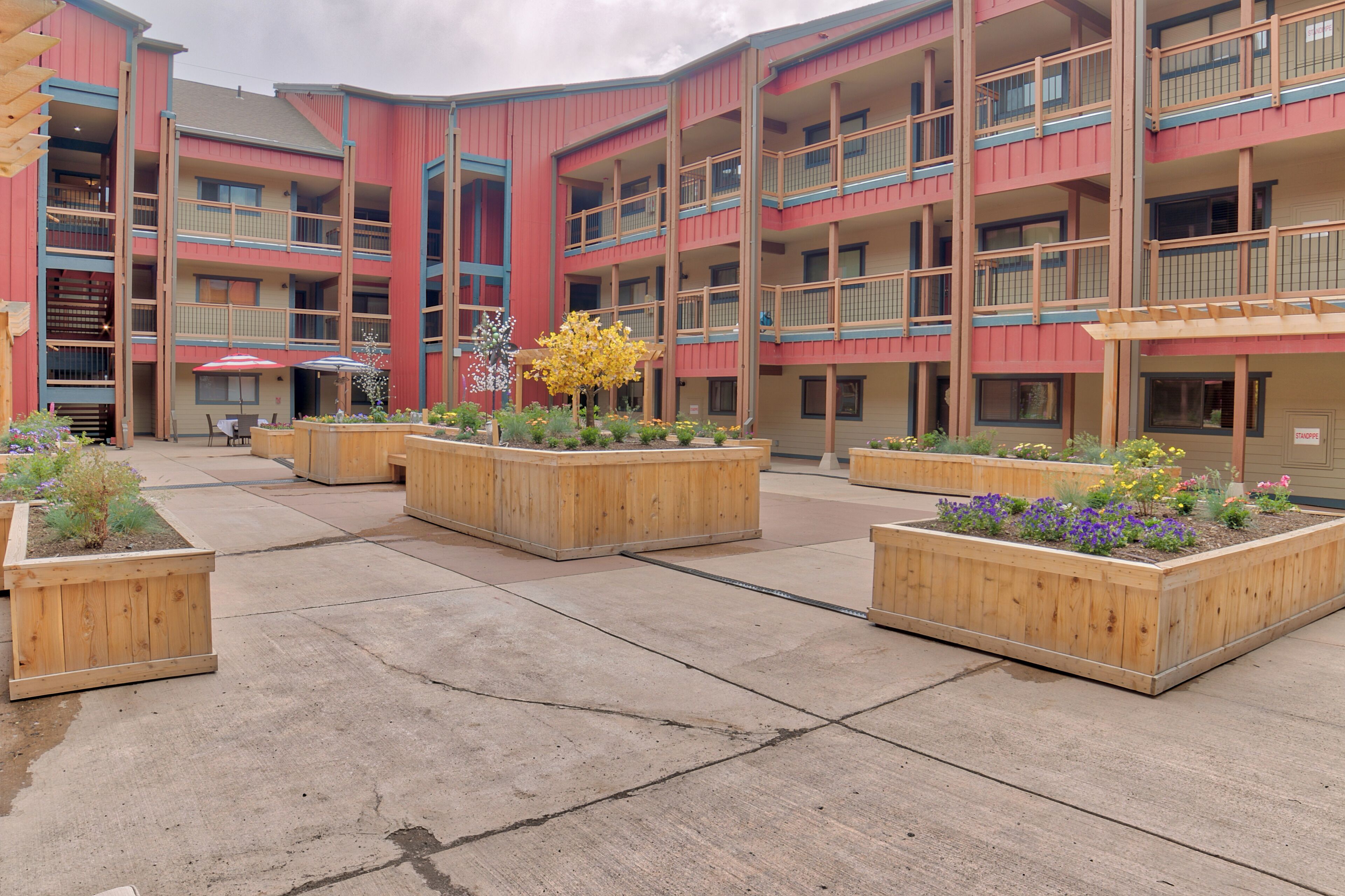 A multi-story building with balconies and a courtyard with wooden planters and flowers.