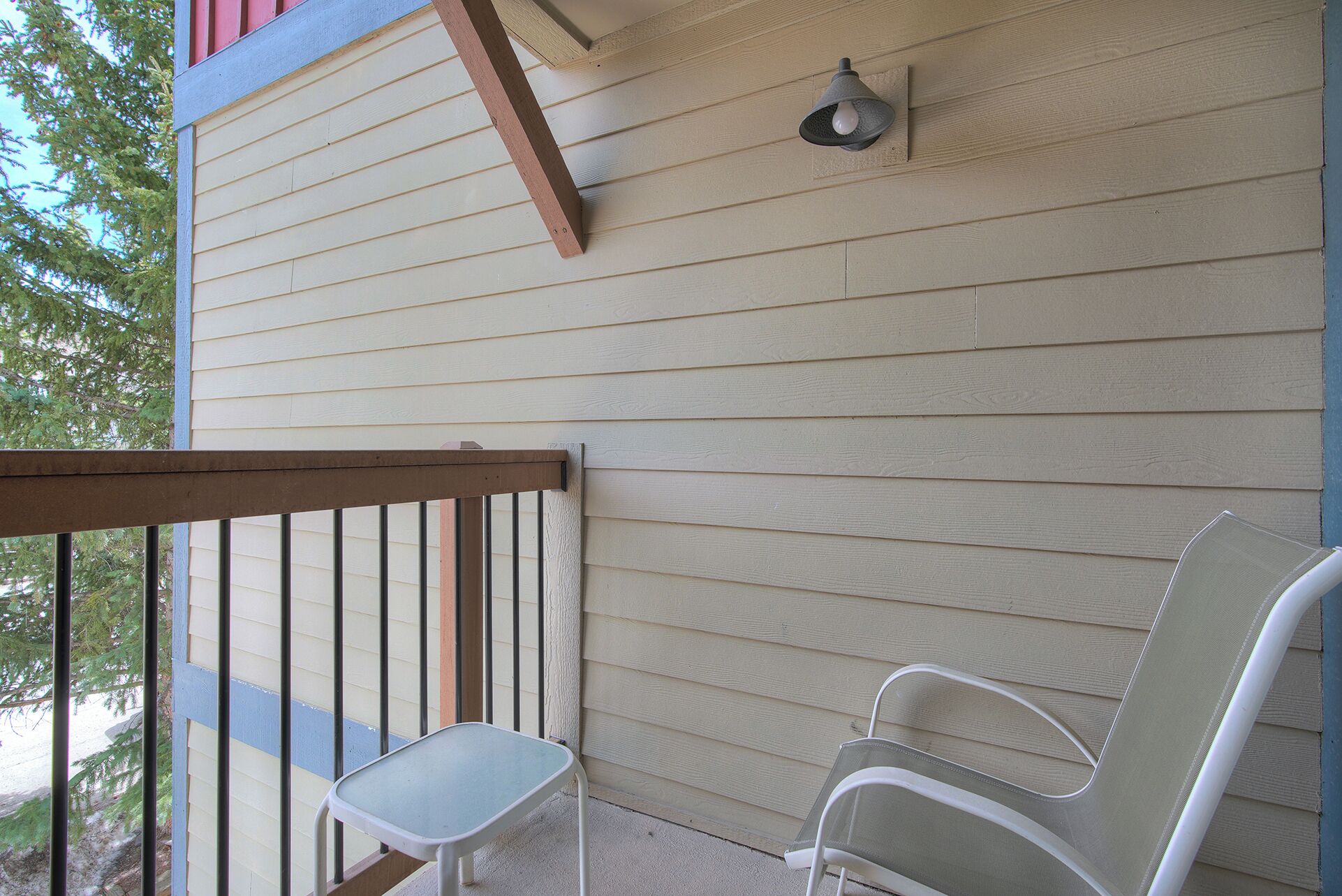 A balcony with a wooden railing, two white chairs, and a wall-mounted light fixture.
