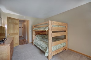 Un lit superposé dans une pièce où se trouvent une commode en bois et une porte donnant sur une autre pièce.