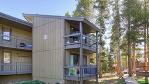 A multi-story building with balconies, a wooden deck, and a forested area. - Gold Camp II E87 Condo (Breckenridge)