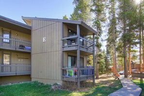 A multi-story building with balconies, a wooden deck, and a forested area. - Gold Camp II E87 Condo (Breckenridge)