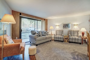 A cozy living room with a sofa, two armchairs, a coffee table, and a rug. There are lamps and a framed picture on the wall.