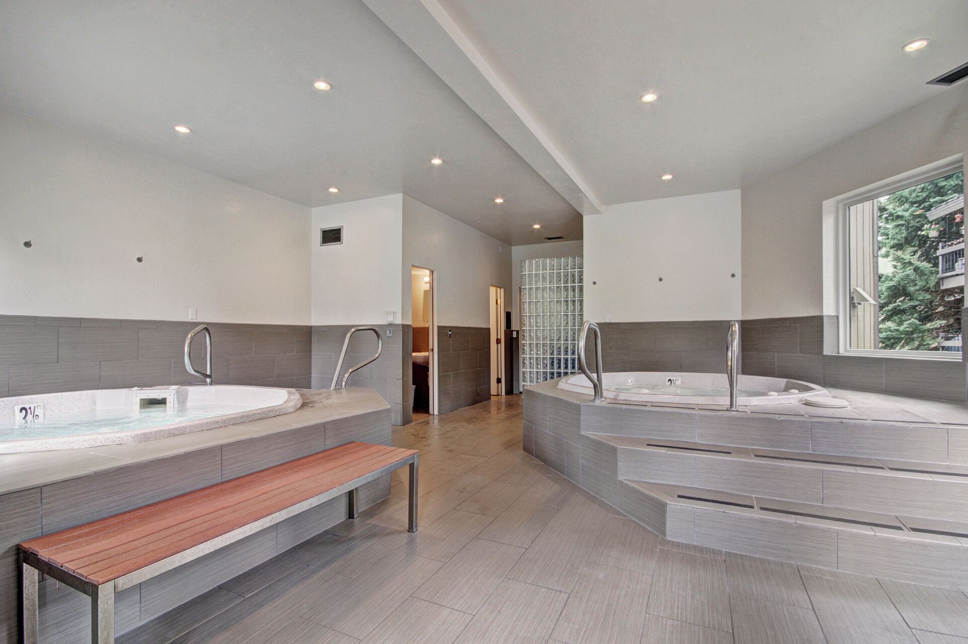 A modern bathroom with two large tubs, a bench, and a glass shower enclosure.