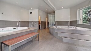 A modern bathroom with two large tubs, a bench, and a glass shower enclosure. - Gold Camp II E87 Condo (Breckenridge)