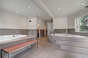 A modern bathroom with two large tubs, a bench, and a glass shower enclosure.