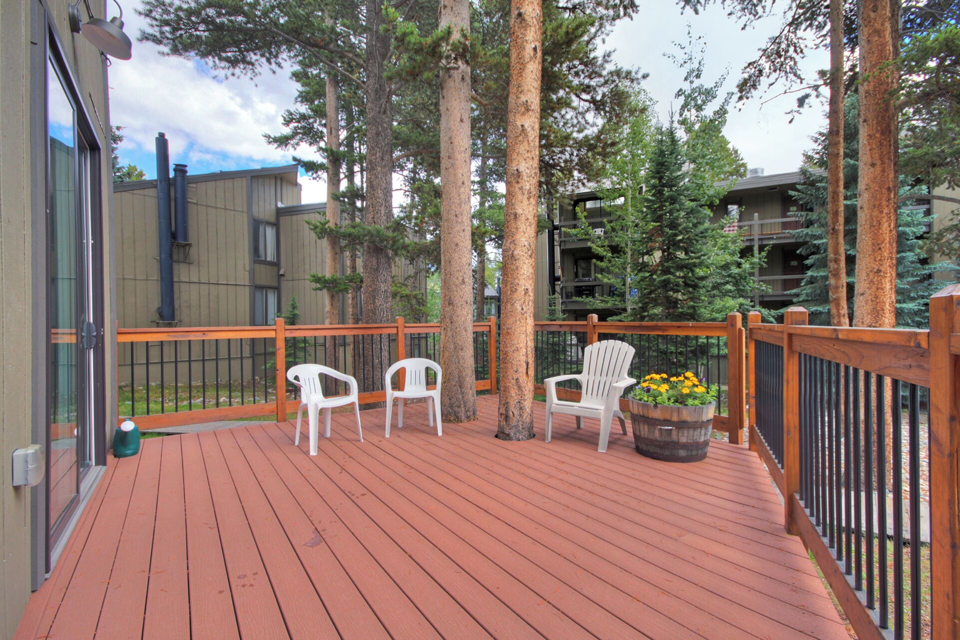 A wooden deck with white chairs and a planter with flowers.