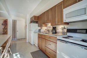 A compact kitchen with wooden cabinets, a white refrigerator, a microwave, a stove, and a coffee maker.
