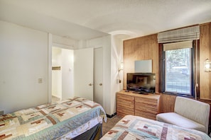 A bedroom with two beds, a dresser, a television, and a window with a view of trees.