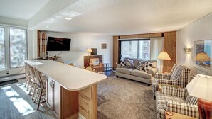 A spacious living area with a kitchen counter, a sofa, and a television. - Gold Camp II E87 Condo (Breckenridge)