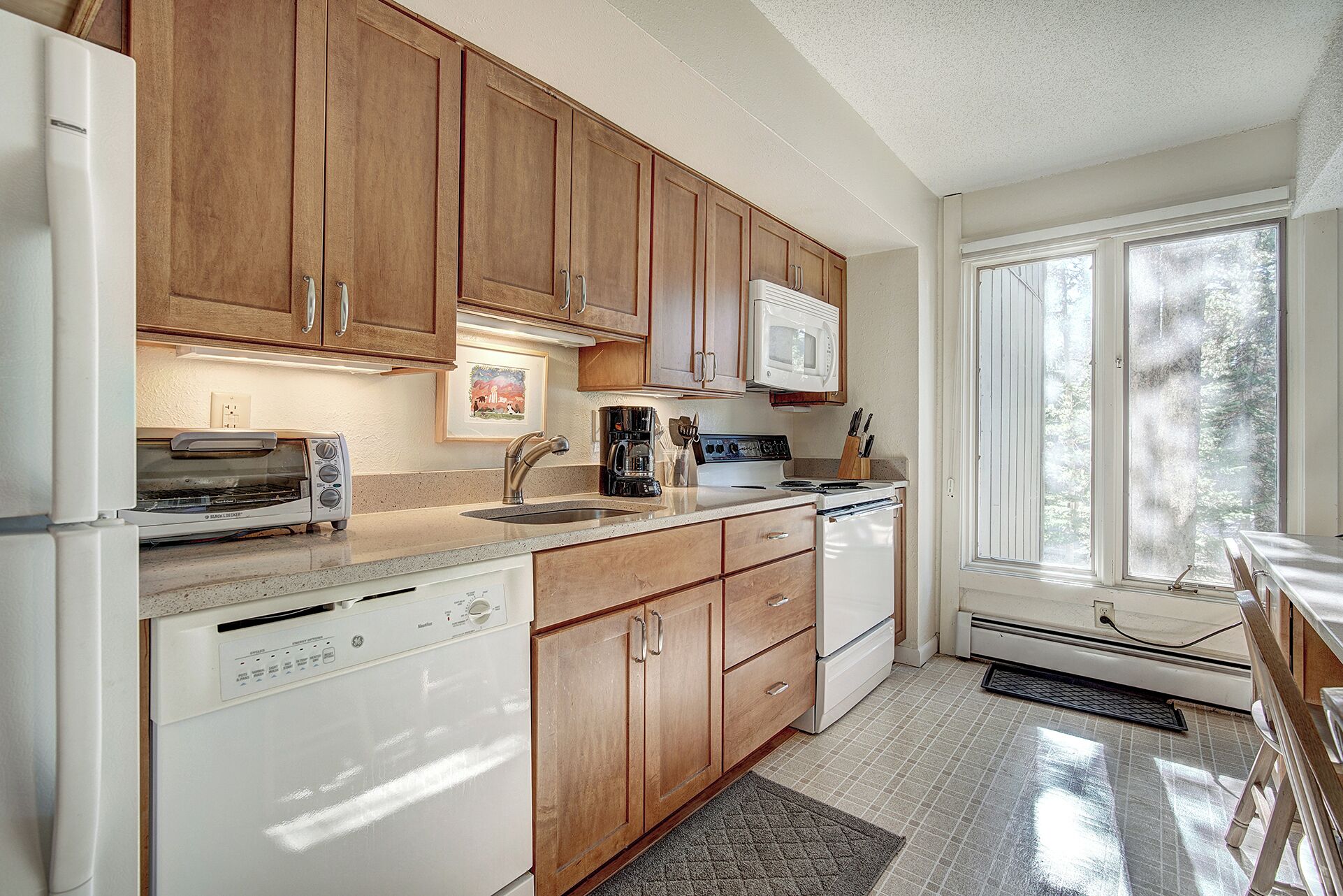 A kitchen with wooden cabinets, a microwave, a dishwasher, and a window with a view of trees.