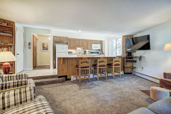 A compact living space with a kitchenette, a dining area with bar stools, and a TV mounted on the wall.
