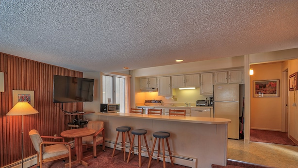 A compact kitchen with a bar area, wooden bar stools, and a dining table. - Gold Camp II E89 Condo (Breckenridge)
