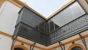 Un balcón en esquina con barandillas de metal ornamentadas y ventanas amplias.