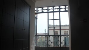 Una habitación con un ventanal grande, un armario oscuro y vistas a un edificio con tejado de tejas.