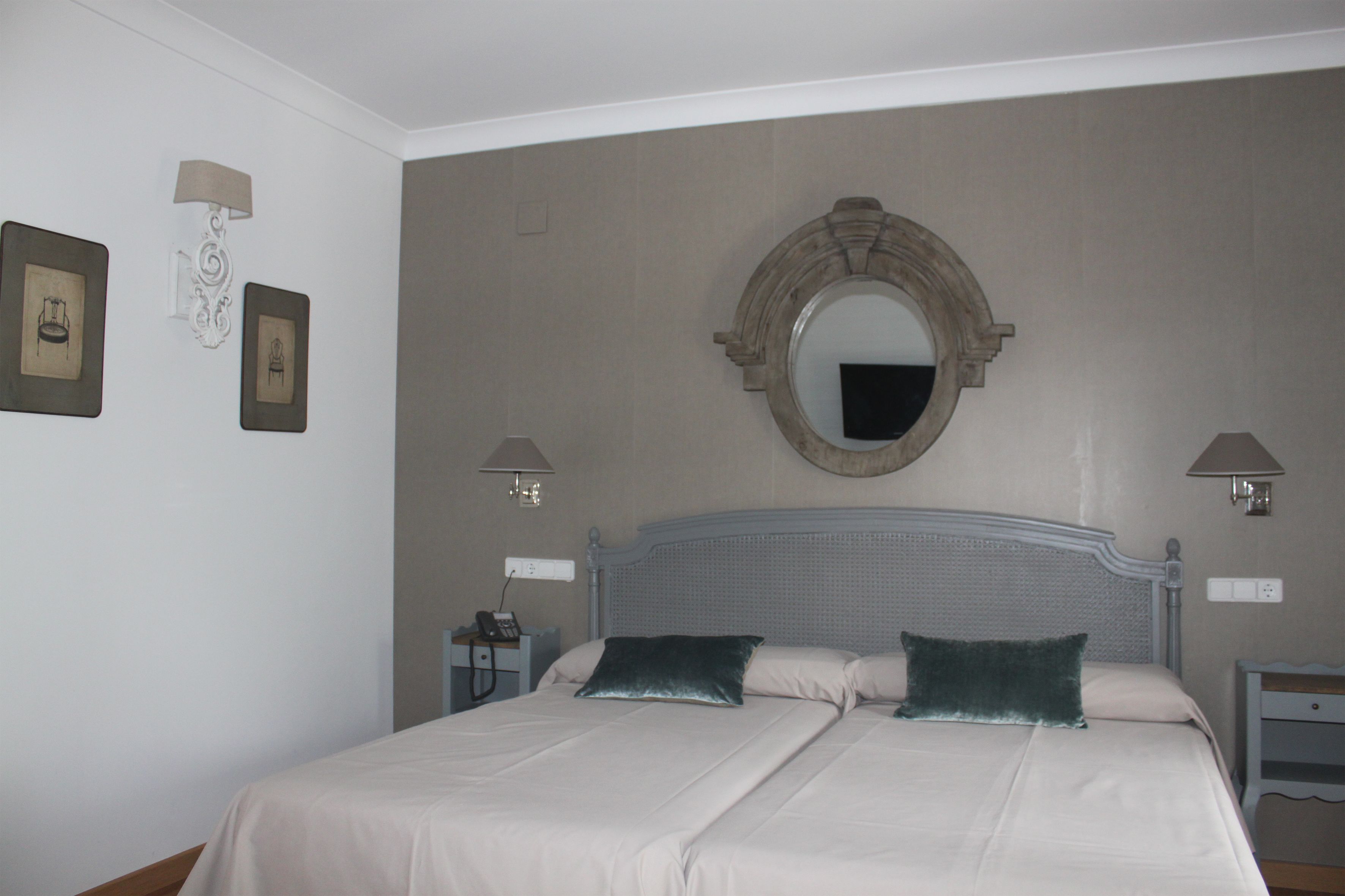 Una cama doble con dos almohadas, una mesita de noche, una lámpara y un espejo fijado a la pared.