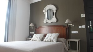 Habitación de hotel con una cama grande, dos mesitas de noche con lámparas, un espejo en la pared y una puerta a la derecha.