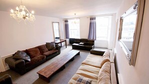 A living room with a brown leather sofa, a beige sofa, a wooden coffee table, and a chandelier. - Edinburgh Princes Street Top Floor Apt (Edinburgh)