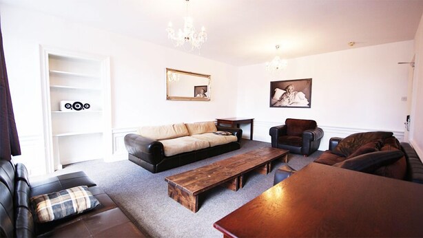 A living room with a sofa, armchairs, a coffee table, and a wooden bench. There are two paintings on the wall and a chandelier. - Edinburgh Princes Street Top Floor Apt (Edinburgh)