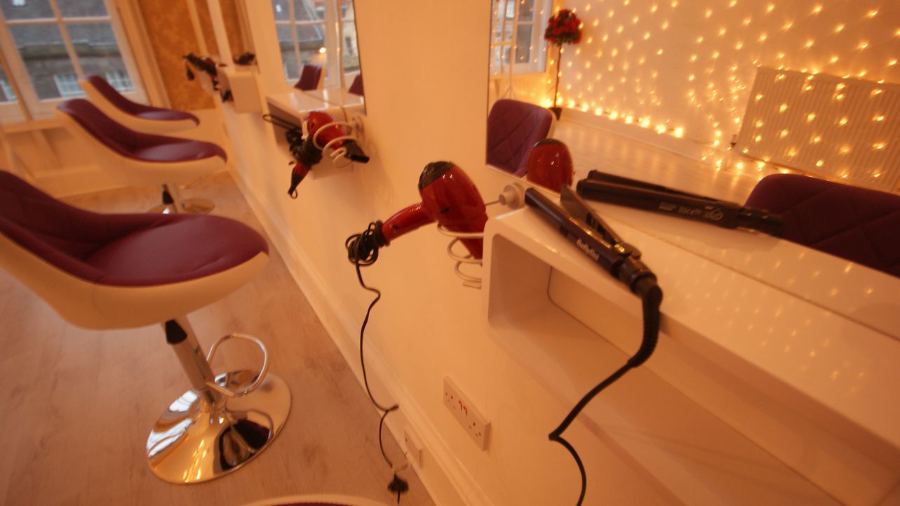 Un salón de belleza con varias sillas rojas y una fila de secadores en un mostrador.