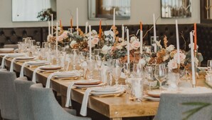 A long dining table set with white plates, glasses, and candles, surrounded by grey chairs. - Casa Basalto (Pachuca)